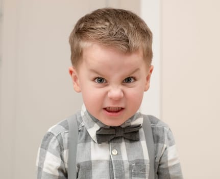 Emotions of anger and anger on a child's face. A small handsome boy, 4 years old, wearing a shirt with a bow tie, shows a grimace with facial expressions. Close-up. portrait