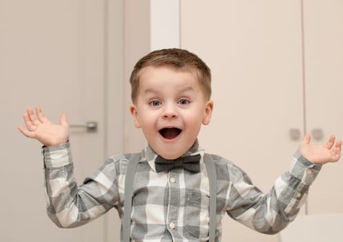 Emotions of surprise and delight on the child s face. A small handsome boy of 4 years old in a shirt with a bow tie shows a grimace with an expression on his face. Close-up. portrait