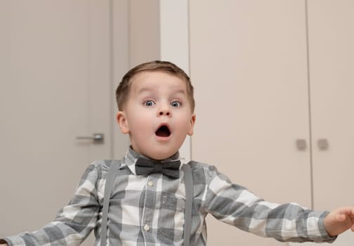 Emotions of surprise and delight on the child s face. A small handsome boy of 4 years old in a shirt with a bow tie shows a grimace with an expression on his face. Close-up. portrait