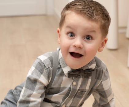 Emotions of surprise and delight on the child s face. A small handsome boy of 4 years old in a shirt with a bow tie shows a grimace with an expression on his face. Close-up. portrait