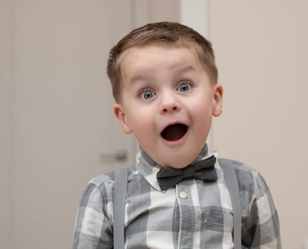 Emotions of surprise and delight on the child s face. A small handsome boy of 4 years old in a shirt with a bow tie shows a grimace with an expression on his face. Close-up. portrait