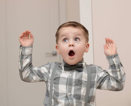 Emotions of surprise and delight on the child s face. A small handsome boy of 4 years old in a shirt with a bow tie shows a grimace with an expression on his face. Close-up. portrait