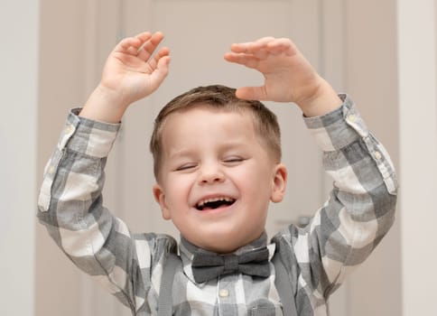 Emotions of happiness, fun, joy and delight on the child s face. A small handsome boy of 4 years old in a shirt with a bow tie shows a mime with a facial expression. Close-up. portrait