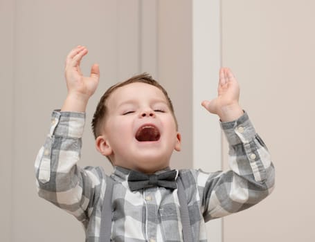 Emotions of happiness, fun, joy and delight on the child s face. A small handsome boy of 4 years old in a shirt with a bow tie shows a mime with a facial expression. Close-up. portrait