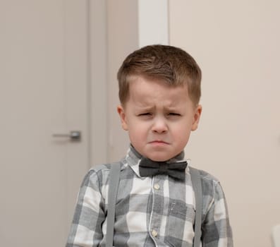 Emotions of sadness, resentment, sadness on the child s face. A small handsome boy of 4 years old in a shirt with a bow tie shows facial expressions. Close-up. portrait