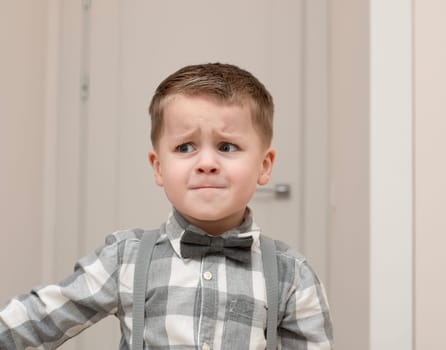 Emotions of sadness, resentment, sadness on the child s face. A small handsome boy of 4 years old in a shirt with a bow tie shows facial expressions. Close-up. portrait