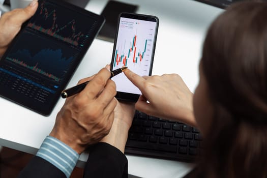 Cropped with focusing on phone with hand pointing with discussing dynamic stock market in two business traders on screens on real time currency rate investment risk data at modern office. Postulate.