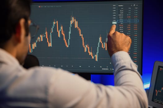 Smart trader businessman concentrating on dynamic stock exchange investment on pc and laptop showing on screen with high profit in searching market at neon light office in dark room night. Surmise.