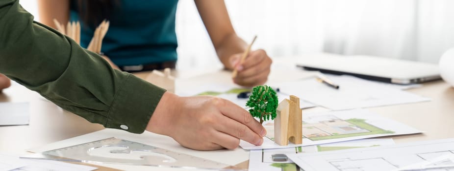 Professional architect team discuss about green design of eco house on meeting table with blueprint and model scatter around. Closeup. Focus on hand. Green city concept. Delineation.