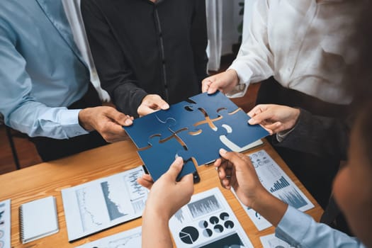 Corporate officer worker collaborate in office, connecting puzzle pieces with report paper on table as partnership and teamwork. Unity and synergy in business concept by merging jigsaw puzzle. Concord