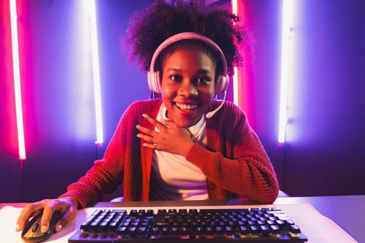 Gaming streamer, African girl playing online fighting with Esport skilled team wearing headphones in neon color lighting room. Talking other players planing strategies to win competitors. Tastemaker.