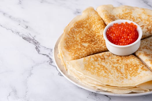 Pancakes with red caviar on a marble table, with copy space for text.