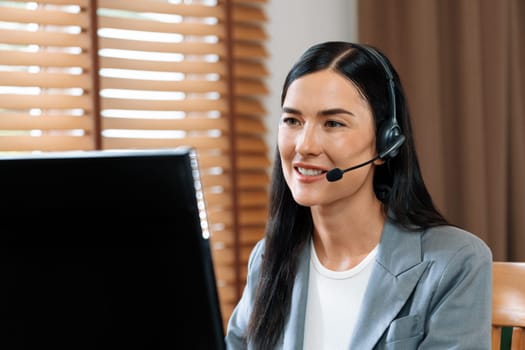 Female call center operator or customer service helpdesk staff working on workspace while talking on the headset to provide assistance for customer. Professional modern business service. Blithe