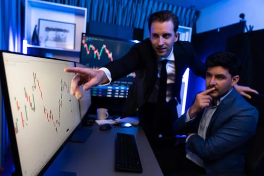 Two stock investors discussing and pointing interesting market stock on monitor. Trend of the technology for dynamic economic investment for planning to select at neon light workplace. Sellable.