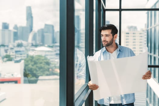 Professional architect engineer or male worker in casual outfit looking at skyscraper and city view while holding project plan. Creative design, civil engineering, building construction. Tracery.