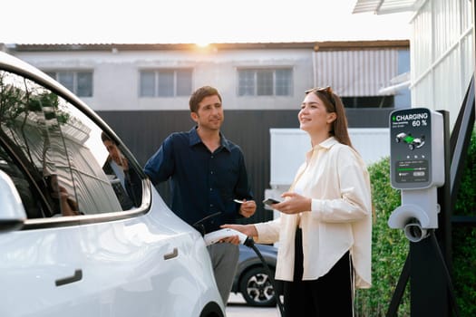 Eco-friendly conscious family couple recharging EV vehicle from home charging station. EV electric car technology utilized as alternative transportation for future sustainability. Expedient