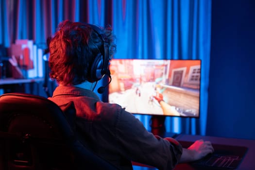 Host channel of young gaming streamer, team gamer playing battle game shooting with multiplayer at warship on pc screen with back side image, wearing headset with mic at digital neon room. Gusher.