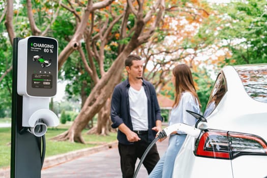 Lovely young couple recharging battery for electric car during autumnal road trip travel EV car in autumnal forest. Eco friendly travel on vacation during autumn. Exalt