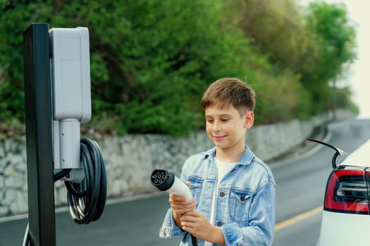 Little boy recharging eco-friendly electric car from EV charging station. EV car road trip travel concept for alternative transportation powered by clean renewable and sustainable energy. Perpetual