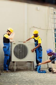 Trained professionals installing condenser for home owner. Qualified technicians commissioned to optimize new HVAC system's performance, ensuring it operates at maximum efficiency