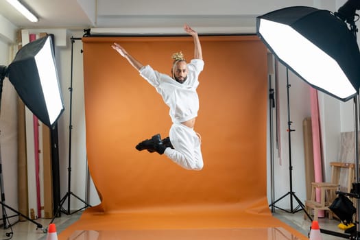 Full length african-american gay man jumping wearing white dancing on orange studio background. Brazilian homosexual male posing in photo studio. Bearded afro-american gay man dancer