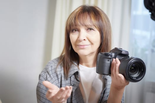 Senior old elderly woman with black camera with a large lens indoors in the studio. Professional photographer. Age Hobby