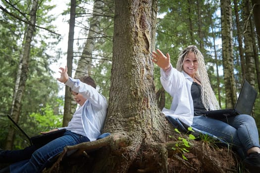 Mother and son with a laptops in the forest in summer. Fat young smart teenage boy and woman working with modern IT technologies in nature