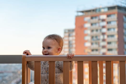 baby smiling cheerfully looks out of the crib against the backdrop of the city landscape.