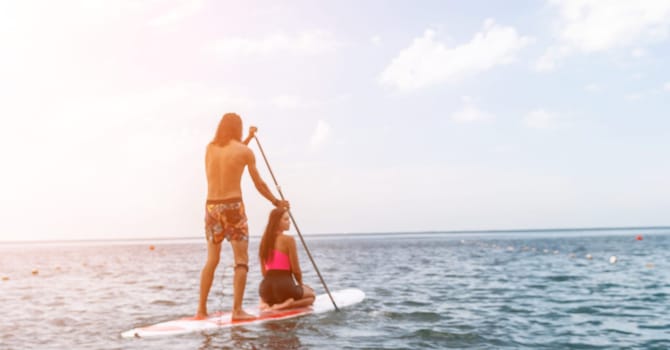 Sea woman and man on sup. Silhouette of happy young woman and man, surfing on SUP board, confident paddling through water surface. Idyllic sunset. Active lifestyle at sea or river