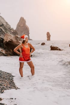 Woman travel sea. Young Happy woman in a long red dress posing on a beach near the sea on background of volcanic rocks, like in Iceland, sharing travel adventure journey