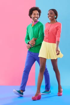 Couple, walk and happy with fashion in studio, background and creative aesthetic. Excited, woman and man together with colorful retro style, unique clothes or person with support, love and trust.