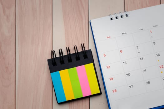 A close up of desk calendar and index sticky note on a wooden table for the concept of important dates, reminders and a well organized workspace.
