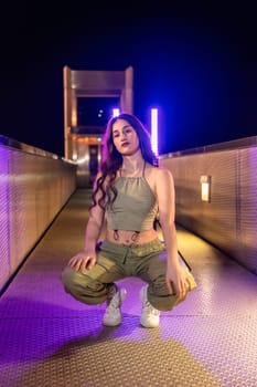 Vertical photo of a young woman hip hop dancer in squatting in a bridge at night
