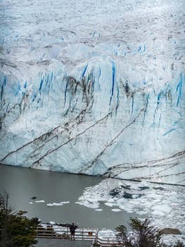 Solo visitor on a platform takes in the view of a glacier and icy sea.