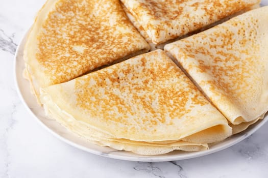 A stack of thin pancakes on a light marble table.