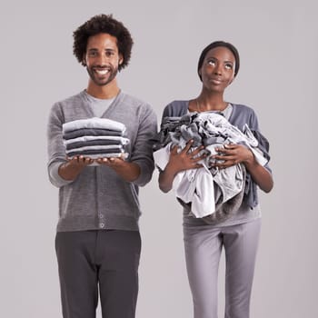 Young, couple and laundry or clothes for helping, support and thinking of house, task or home management in studio. African man and woman with domestic ideas for gender equality on a gray background.