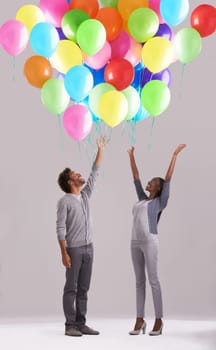 Happy couple, party and celebration with balloons for event, birthday or romance on a gray studio background. Excited man and woman with colorful blowups of helium for date, giveaway or anniversary.