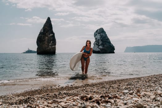 Close up shot of beautiful young caucasian woman with black hair and freckles looking at camera and smiling. Cute woman portrait in a pink bikini posing on a volcanic rock high above the sea