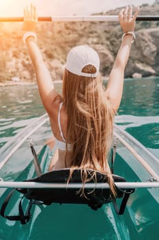 Woman in kayak back view. Happy young woman with long hair floating in transparent kayak on the crystal clear sea. Summer holiday vacation and cheerful female people having fun on the boat.