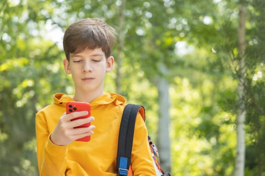 Young boy with dressed yellow hoodie looking at his mobile phone, outdoors spring time