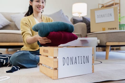 Young Asian women sit in living room sorting clothes for donation in a donation box second hand clothes.