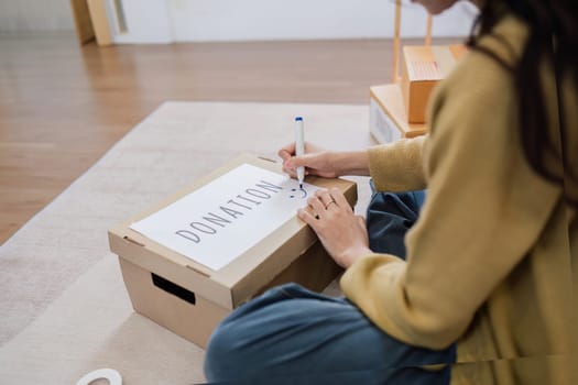 Asian woman sitting and writing on a box to prepare for donation. Help poor people.