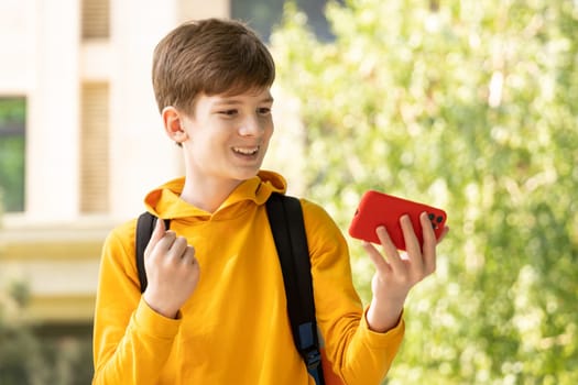 Excited happy teenager boy winner feeling joy smiling and looking at smartphone. Boy using phone, winning lottery game, getting cashback, online gift in app, holding cell phone outdoor