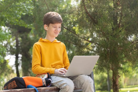 Smiling teenager boy working on laptop. Holding and using a laptop for networking on a sunny spring day, outdoors