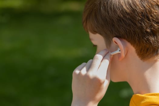 Close up of teenager boy using earbuds outdoor. Lifestyle boy wearing wireless earphones, listening song or audiobook on smartphone, copy space