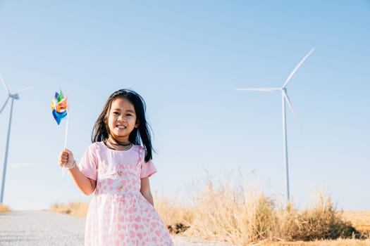 Child's playful joy by windmills, little girl holding pinwheels runs freely. Education through playful wind energy exploration promoting clean electricity and sustainable industry.