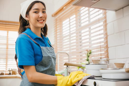 Woman protective gloves cleaning gas stove in kitchen. Wiping dust with cloth emphasizing hygiene and house care. Cleaner at work safety glove hygiene routine. Maid Cleaning housekeeping concept.