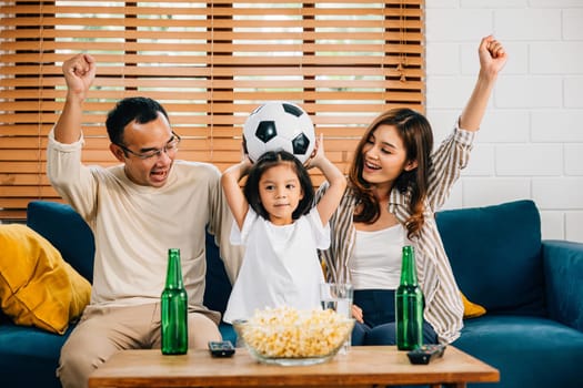 In the warmth of their home, parents and children watch a football match with popcorn and a ball, celebrating a goal. Their togetherness, smiles, and cheers reflect the joy of winning.