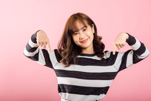 A happy Asian woman, in a portrait, smiles while making a two-finger pointing gesture downward. Studio shot isolated on pink with copy space, perfect for advertisements.