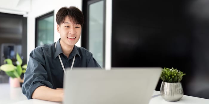 Businessman using laptop computer in office, Happy young asian businessman in modern office looking on laptop.